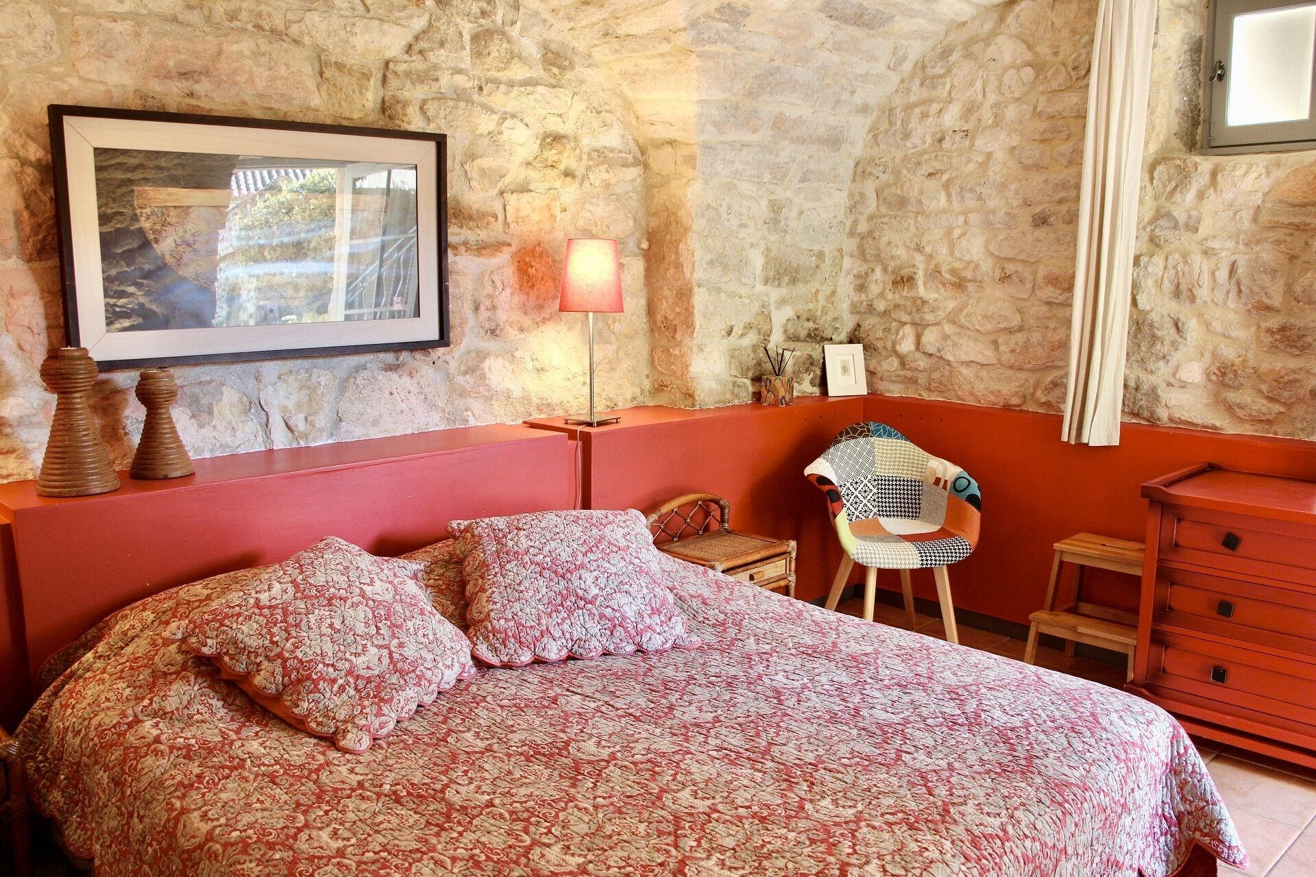 A bedroom with a bed, a chair, a dresser, and a wall-mounted lamp.