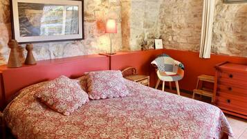 A bedroom with a bed, a chair, a dresser, and a wall-mounted lamp.