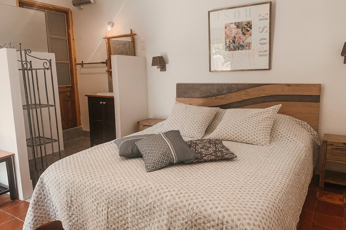 Un dormitorio con cama, almohadas, cabecera de madera, un cuadro en la pared y una mesita de noche.
