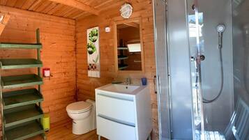 A wooden cabin bathroom with a toilet, sink, and shower.