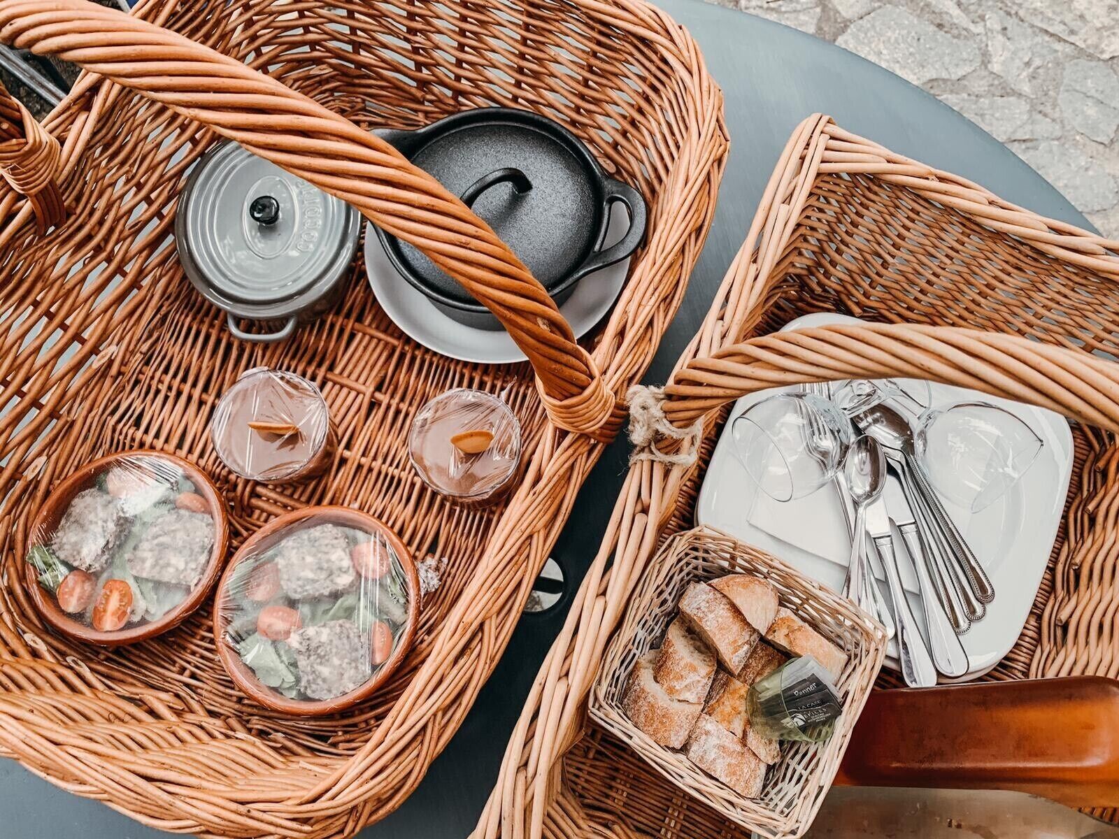 A wicker picnic setup with a pot, cups, bread, and utensils.