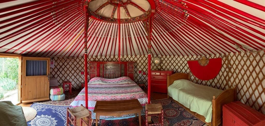 A traditional yurt with a wooden bed, a small table, and a red and white striped canopy.