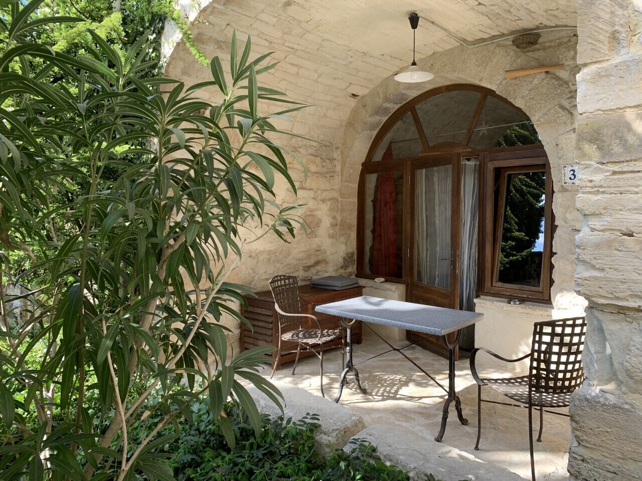 Une terrasse extérieure avec une table et deux chaises, un mur en pierre et une porte en bois.