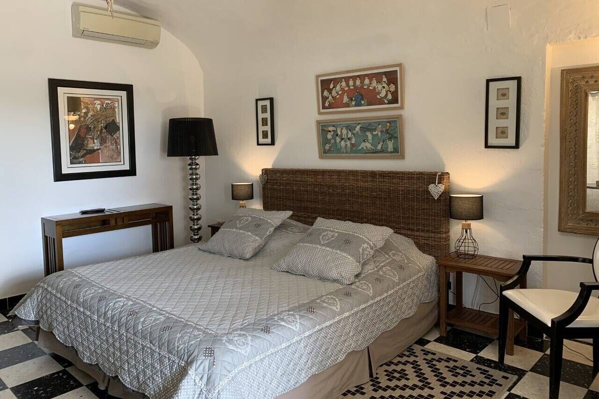 Un dormitorio ordenado con una cama grande, una mesita de noche con una lámpara, una silla y cuadros enmarcados en las paredes.