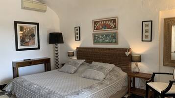 Une chambre à coucher bien rangée, avec un grand lit, une table de chevet avec une lampe, une chaise et des tableaux encadrés accrochés aux murs.
