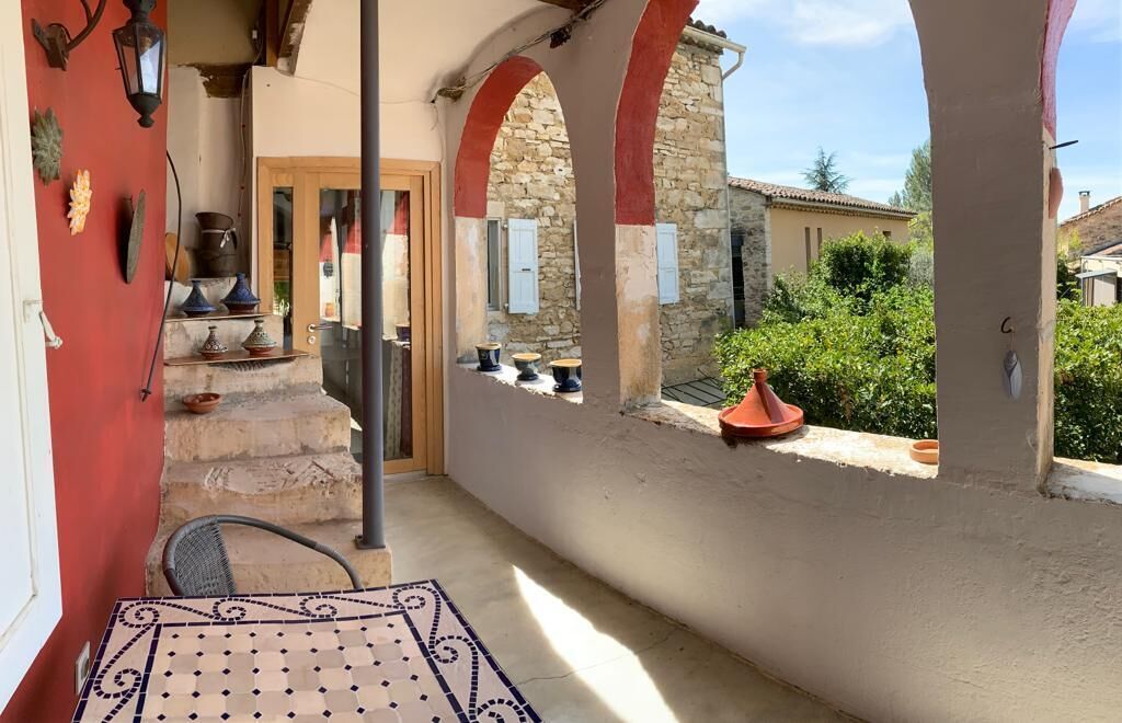 Un espacio al aire libre techado con una mesa de baldosas, una silla y una pared de piedra con una puerta.