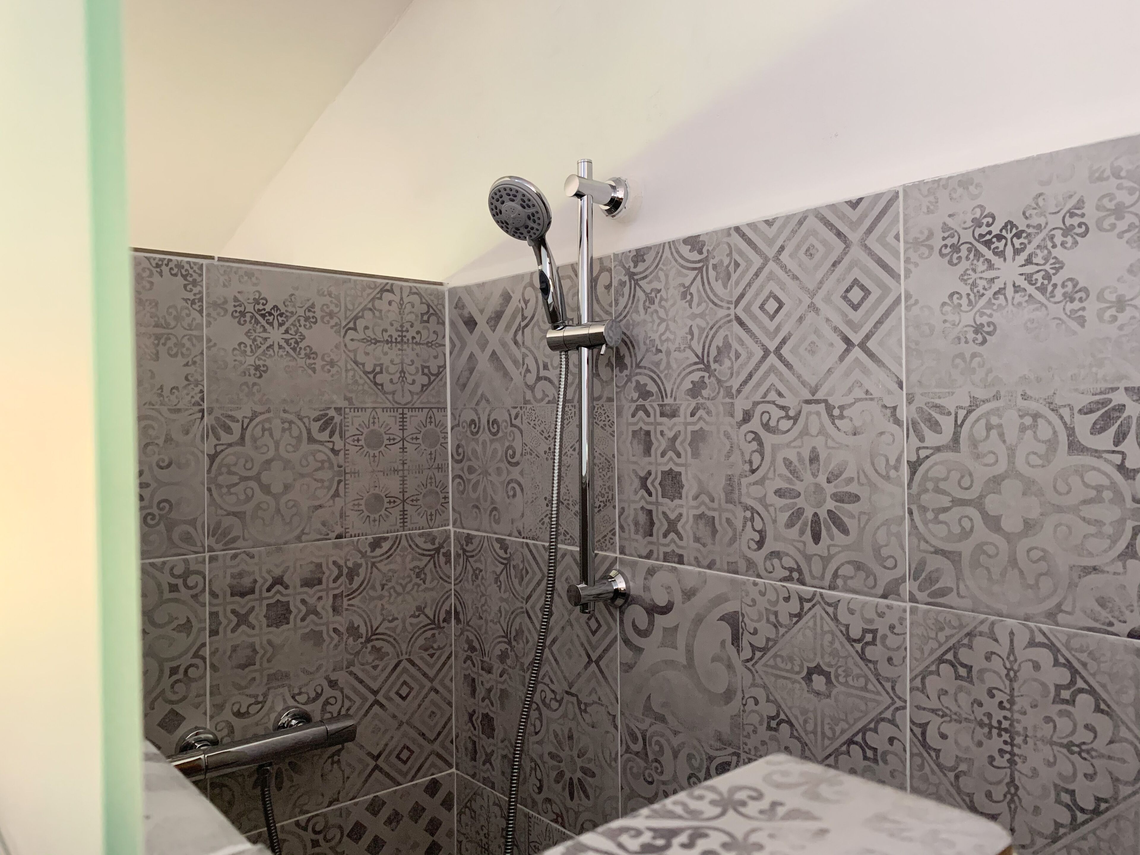 Ducha con cabezal de ducha manual y grifo empotrado, revestida con azulejos estampados.