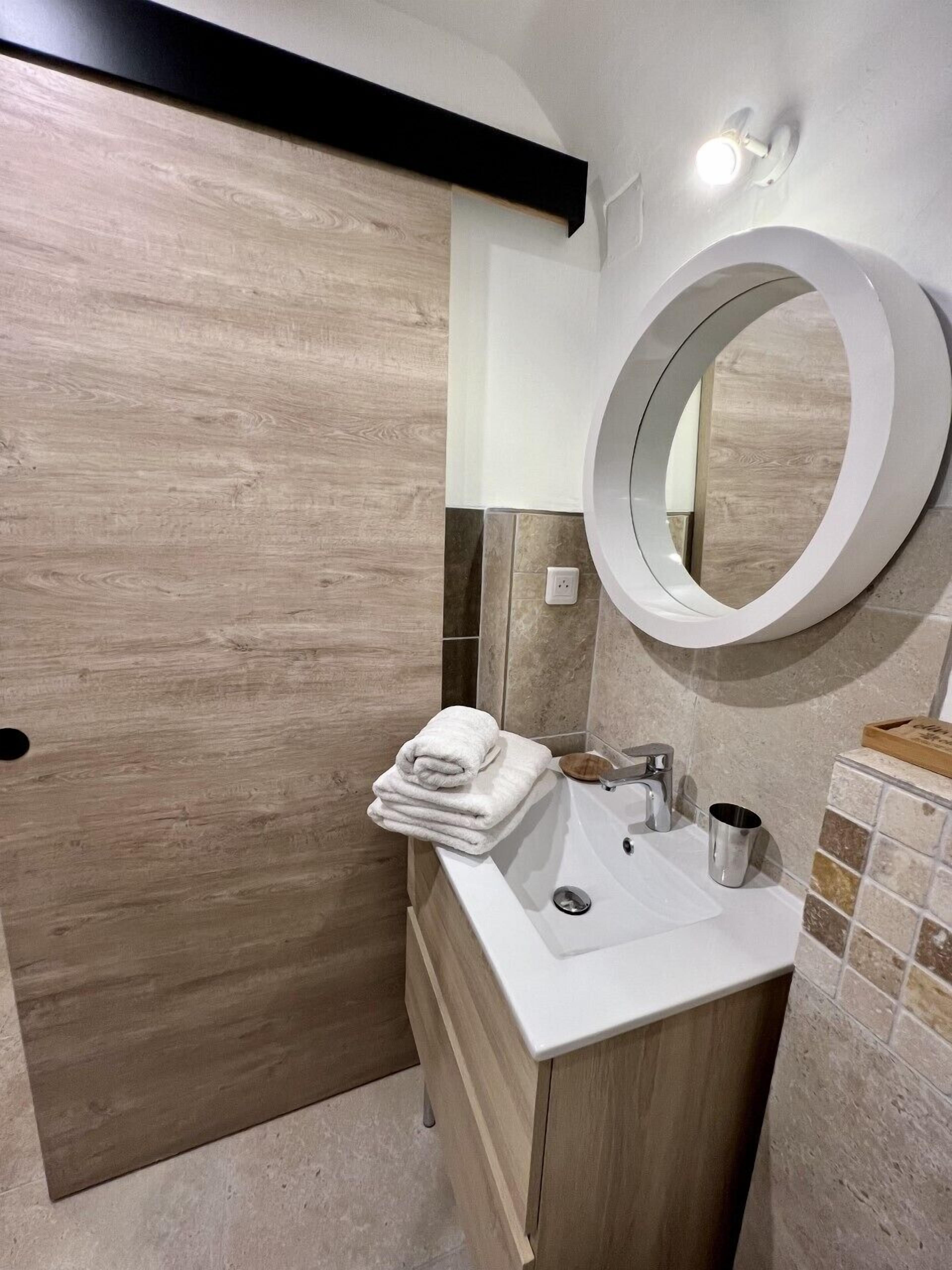 A modern bathroom with a wooden vanity, a round mirror, and a white sink.