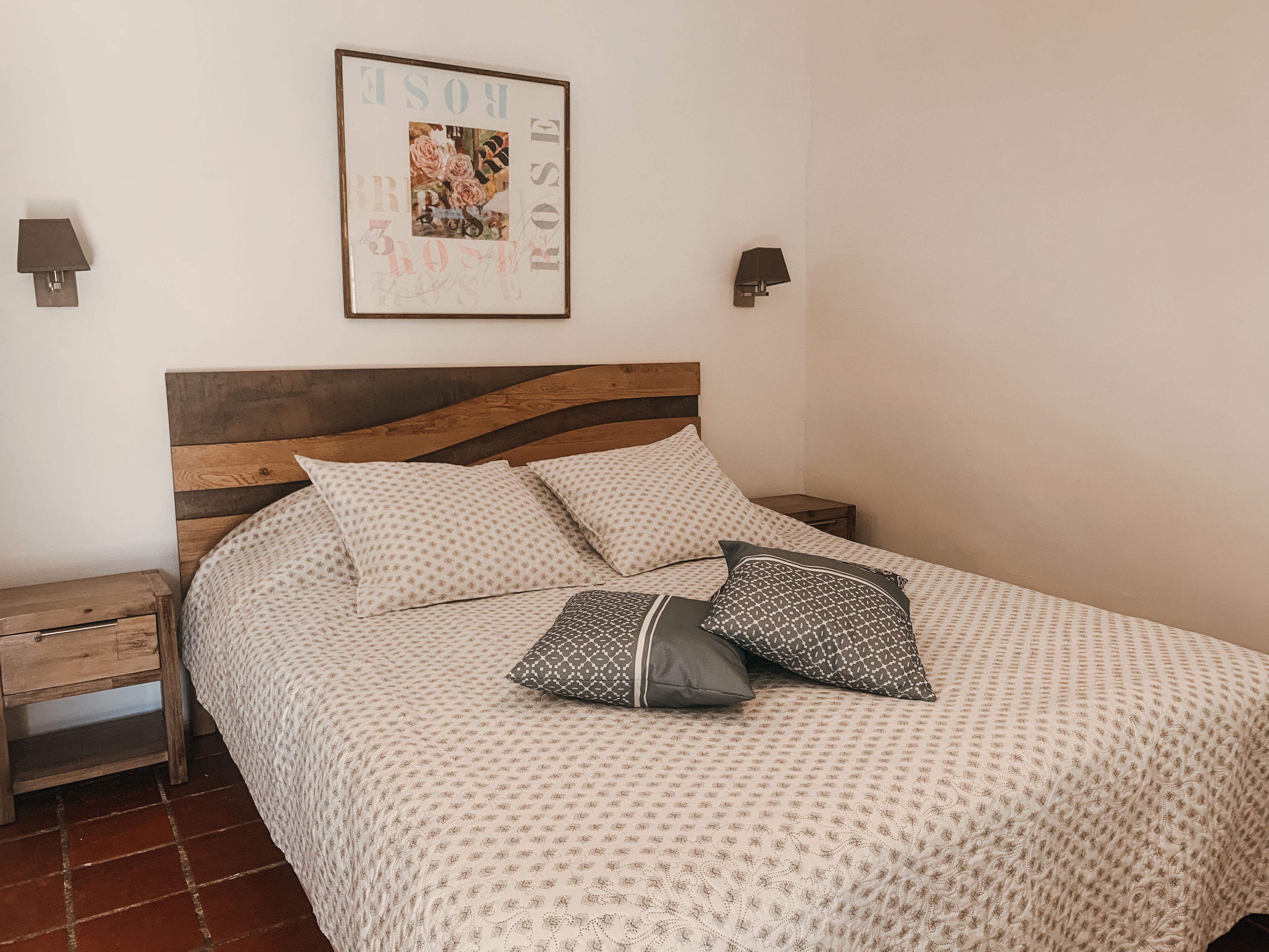 A neatly made bed with patterned bedding, a wooden headboard, and a framed picture above it.