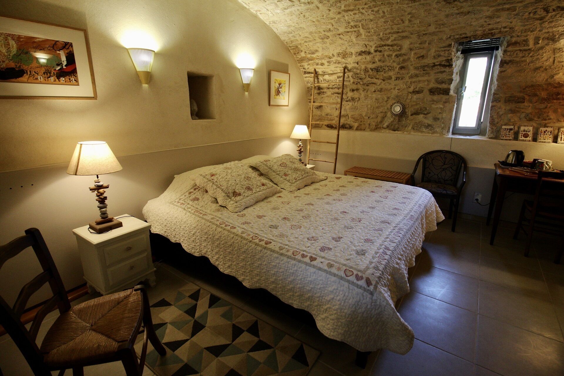 A bedroom with a bed, two wall-mounted lamps, a chair, a desk, and a window with a view.
