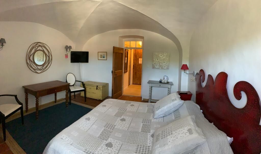 A bedroom with a bed, a desk, a chair, a television, and a door leading to another room.