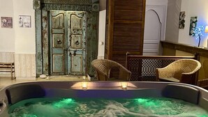 A hot tub with two lit candles, wicker chairs, and a rustic door. - Mas Escombelle Chambre d'Hôte (Barjac)