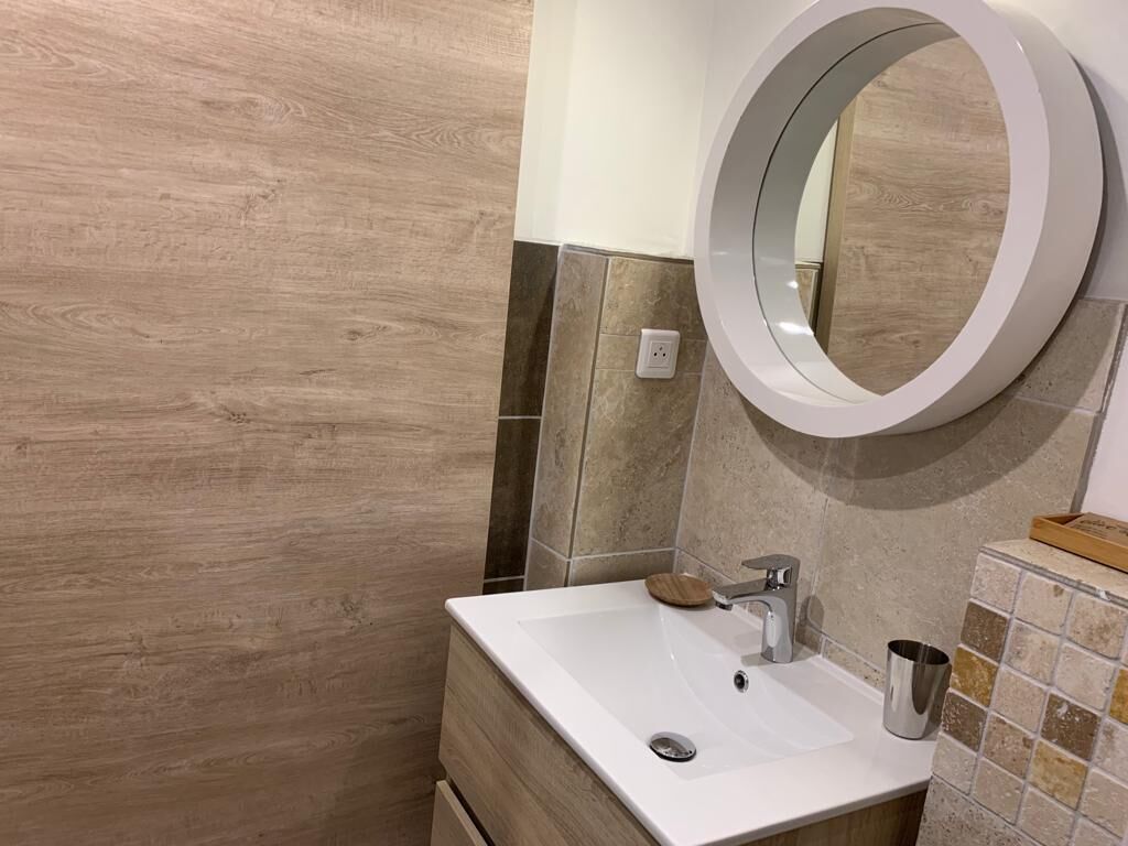 Un baño con pared de madera, un lavamanos blanco con grifo moderno y un espejo redondo.