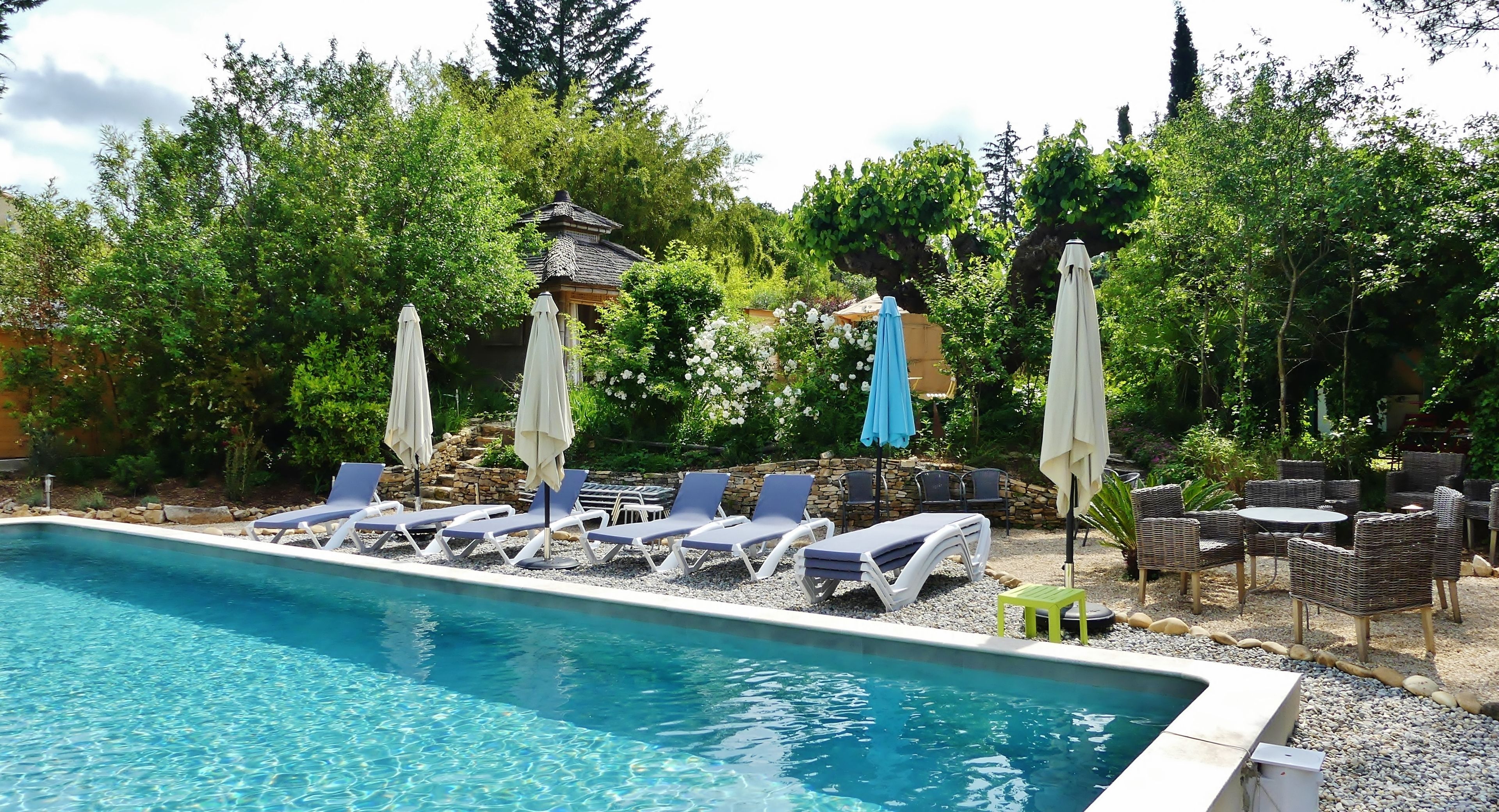 A swimming pool with lounge chairs and umbrellas, surrounded by greenery and stone walls.