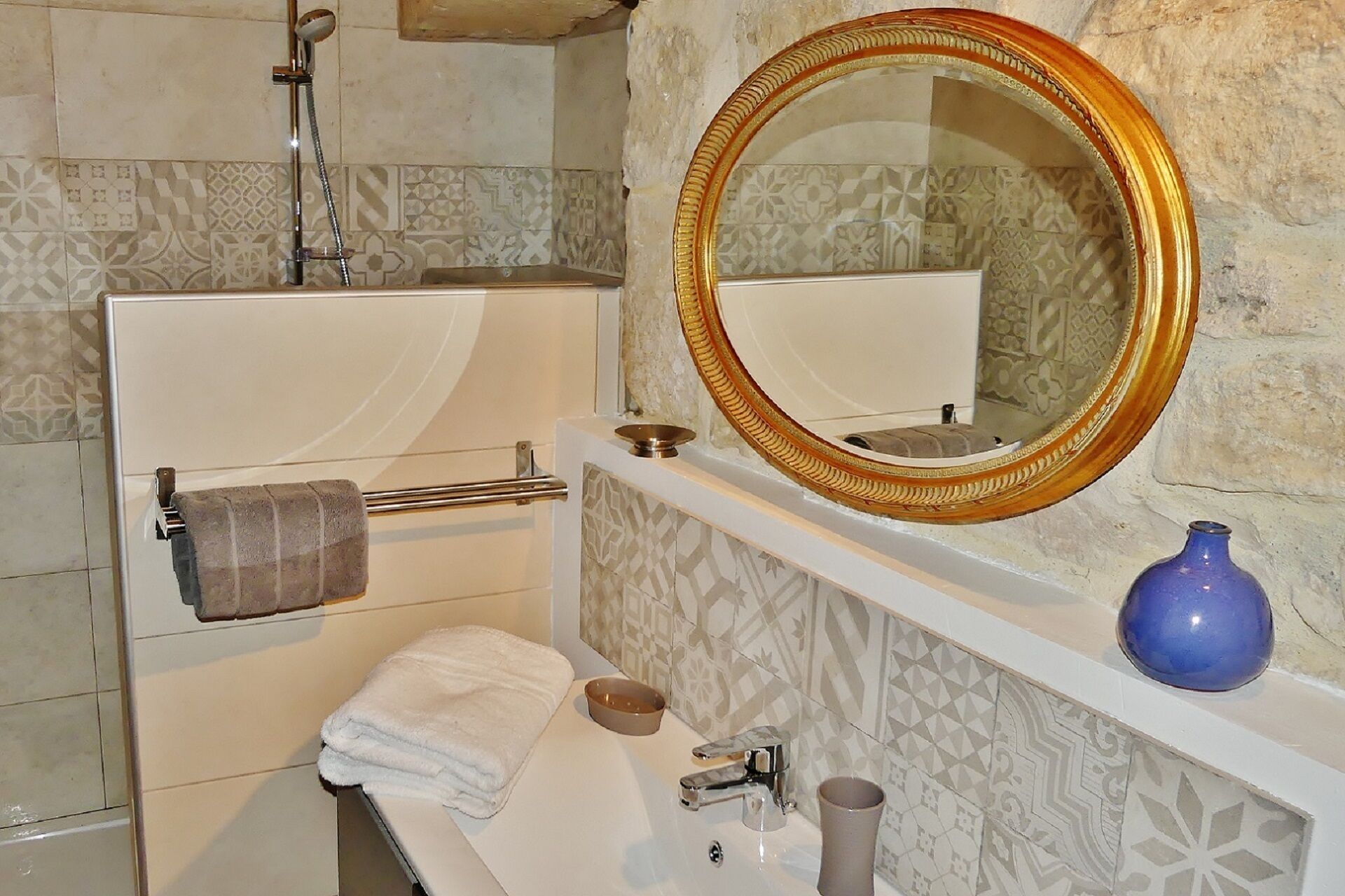 Ein Badezimmer mit einem weißen Waschbecken, einem Spiegel mit goldener Rahmung, einem Handtuchhalter und einer blauen Vase auf der Ablagefläche.
