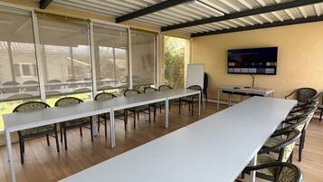 Ein Konferenzraum mit langem Tisch, Stühlen, einer Tafel und einem Fernseher an der Wand.