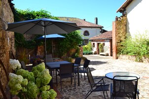 An outdoor patio with a table and chairs, a large umbrella, and potted plants.