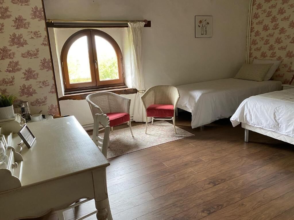 A room with a wooden floor, a desk with a chair, two beds, and a window with curtains.