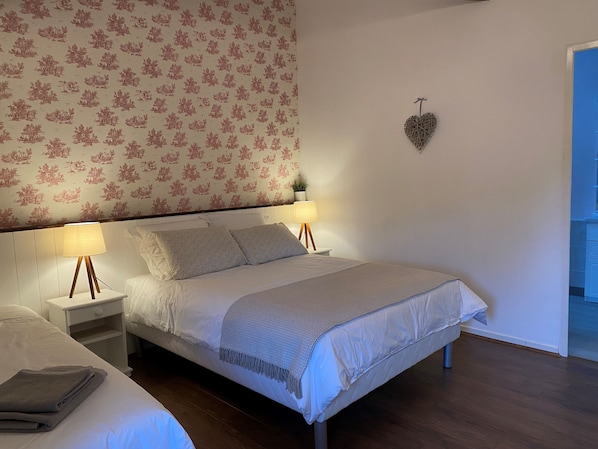 A neatly made bed with a patterned headboard, two bedside lamps, and a heart-shaped decoration on the wall. - L'Envers (Abzac)