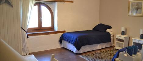 A bedroom with a bed, a window with curtains, a bedside table, a chair, and a rug.