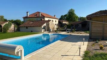 A swimming pool with a tiled deck, surrounded by houses with red-tiled roofs.