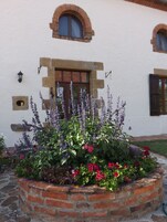 A garden bed with lavender and red flowers in front of a white building with a brick arch window and a door.