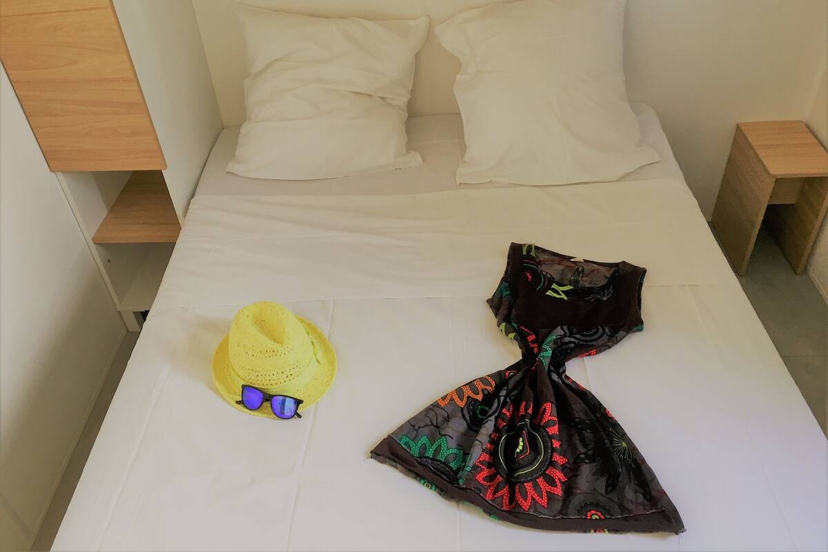 A bed with white bedding, a yellow hat, and a black patterned scarf on it.