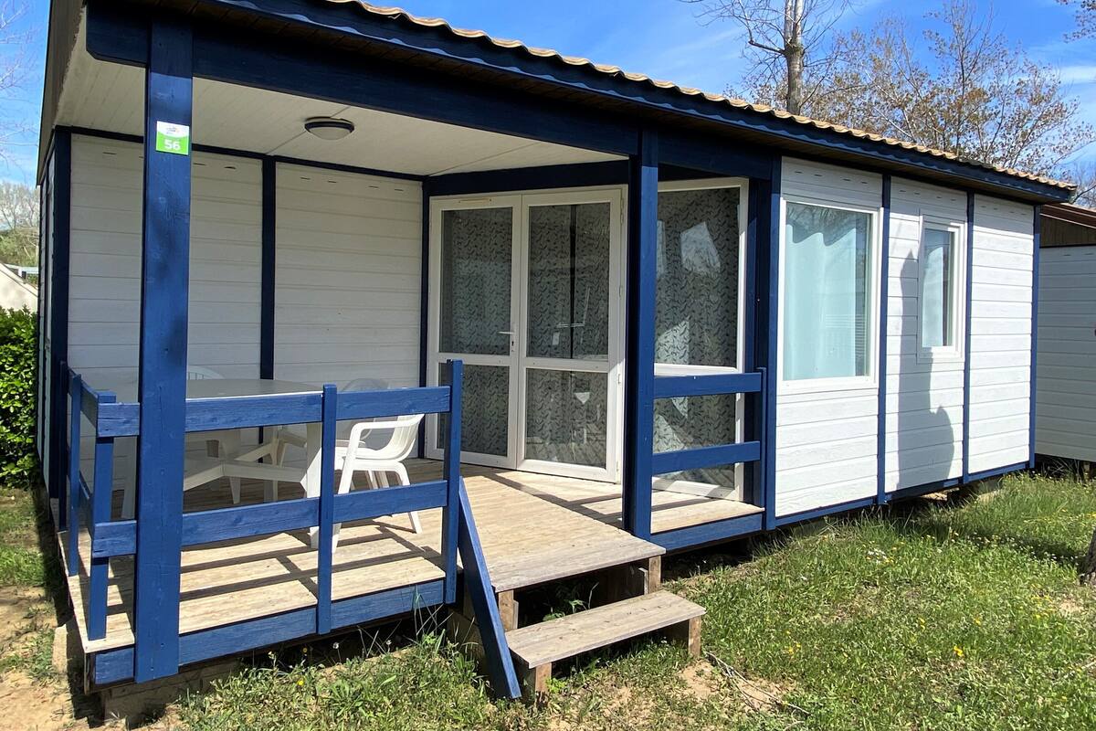 A small, single-story cabin with a porch, a covered outdoor seating area, and a sliding glass door.