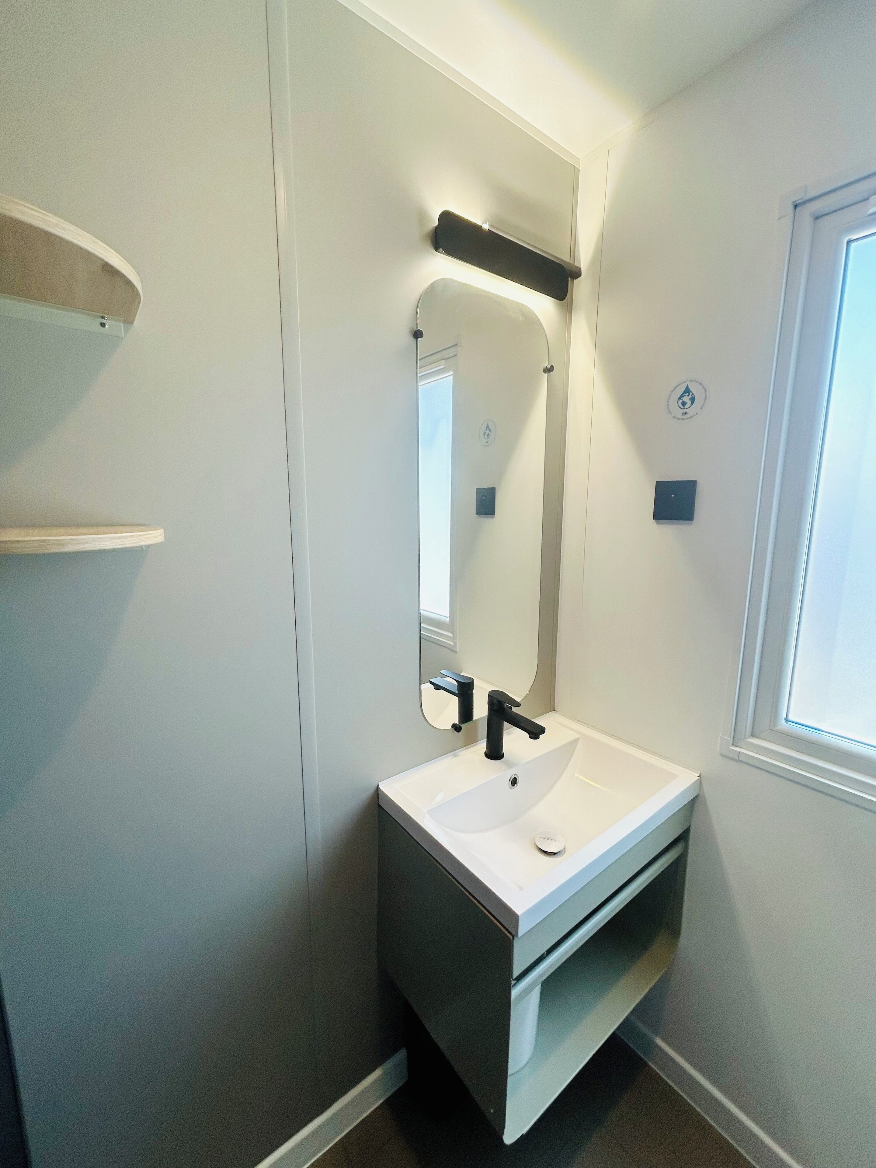 Un baño moderno con un lavamanos blanco, grifo negro y un espejo grande.
