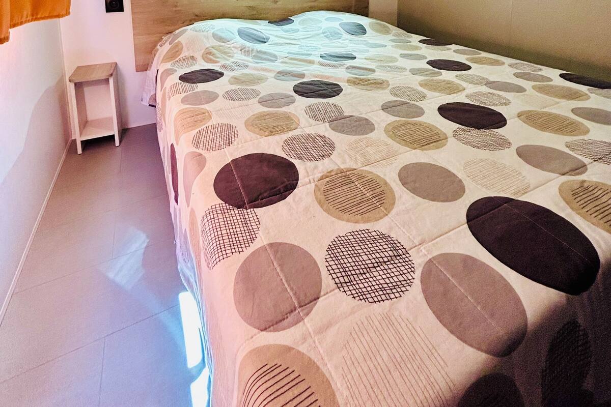 A bedroom with a bed, a wooden headboard, a small nightstand, and a shelf above the bed.