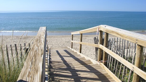 Una passerella in legno conduce a una spiaggia, con una vista libera sull'oceano.