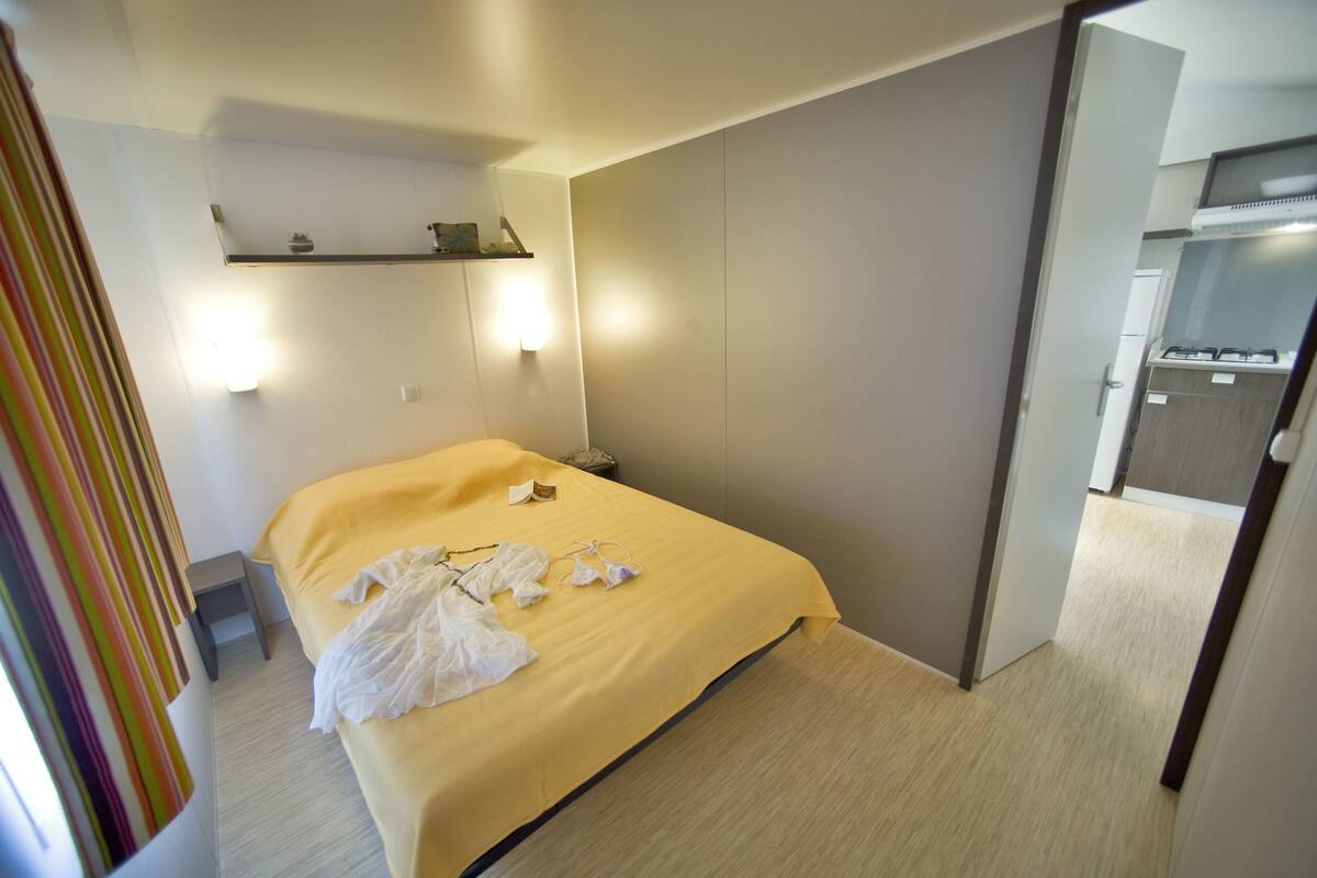 A hotel room with a bed, bedside table, and a small shelf with a lamp.