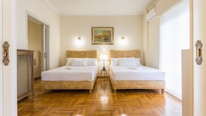 A hotel room with two beds, a wooden floor, a painting on the wall, and a door with a decorative handle. - Victoria Queens Paradise Apartments (Athens)