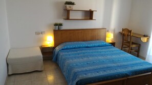 A bedroom with a wooden bed, two bedside lamps, a small table, and a shelf with plants. - B&B Gelsimori (Otranto)