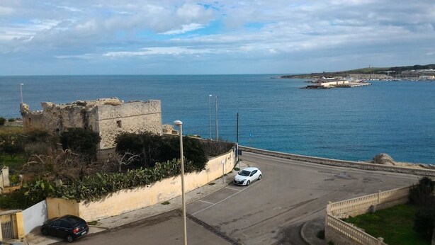 A coastal road with a historic stone wall and a white car parked on the side. - B&B Gelsimori (Otranto)