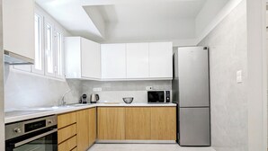 Uma cozinha moderna com armários brancos, geladeira de aço inoxidável, micro-ondas e forno embutido.