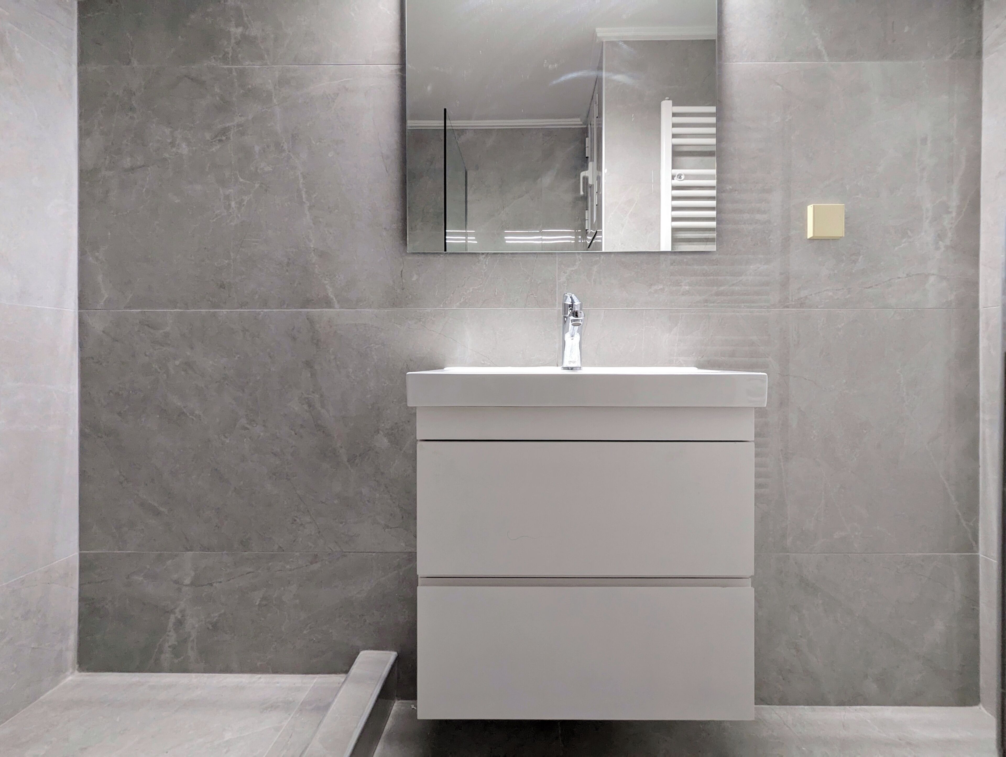 A modern bathroom with a white vanity, a mirror, and a towel rack.