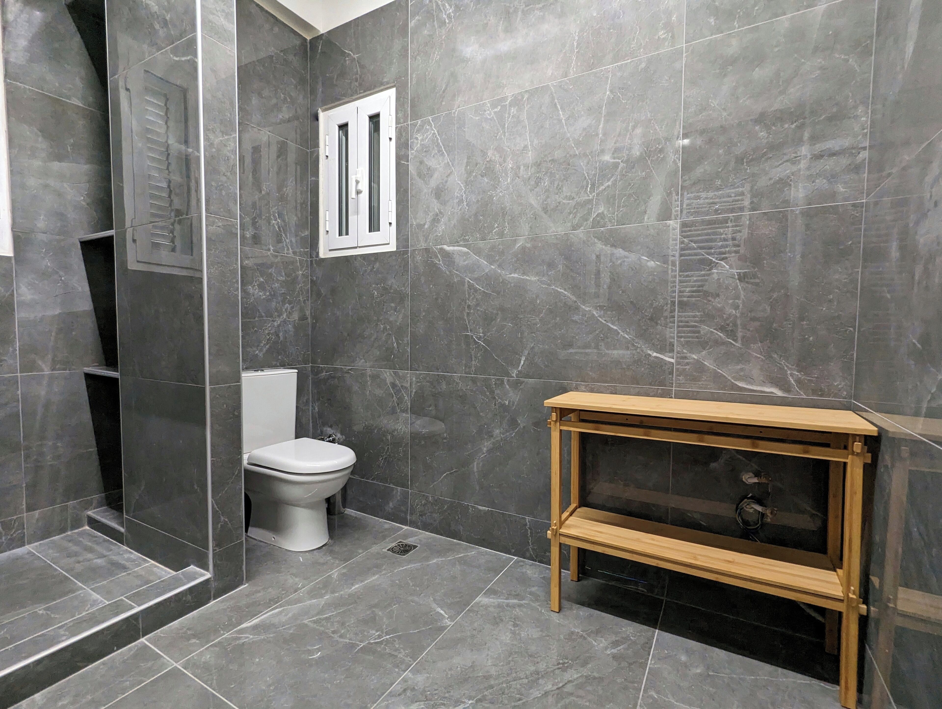 A bathroom with dark marble tiles, a white toilet, and a wooden vanity with a mirror.