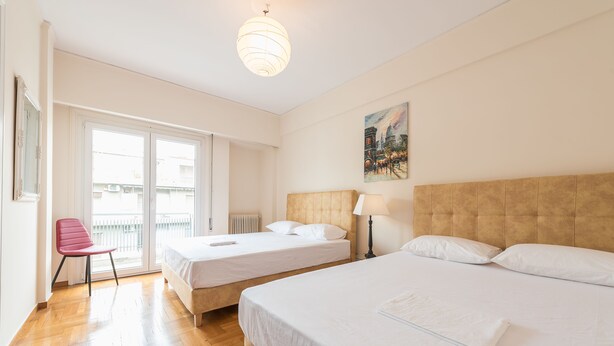 A hotel room with two beds, a chair, a painting, and a view through a sliding door. - Athens Crown Paradise Apartments (Athens)