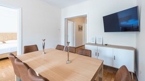 A modern dining area with a wooden table and leather chairs, a flat-screen TV on the wall, and a view into another room. - Athens Crown Paradise Apartments (Athens)