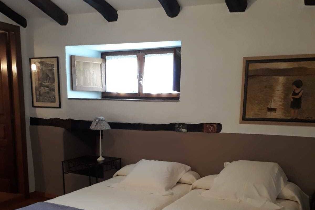 Una cama doble con cabecera, una mesita de noche con lámpara, una ventana con cortinas y un cuadro en la pared.