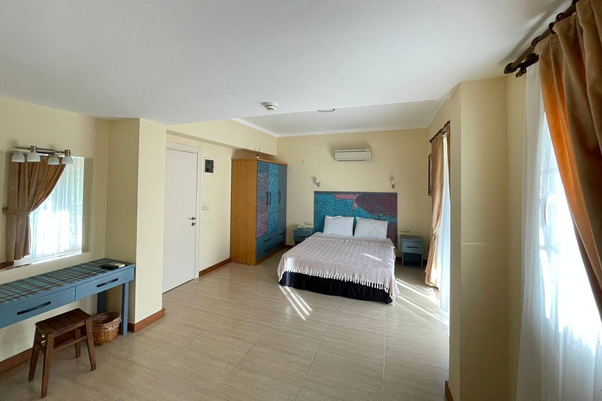 A bedroom with a bed, a desk, a wardrobe, and a window with curtains.