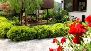 Un jardin avec un belvédère, une table à manger et des chaises. On y trouve également un bâtiment avec une fenêtre et une porte.