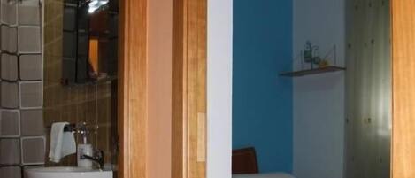 Een badkamer met een wastafel, spiegel en betegelde wanden. Een slaapkamer met twee bedden, voorzien van blauw beddengoed.