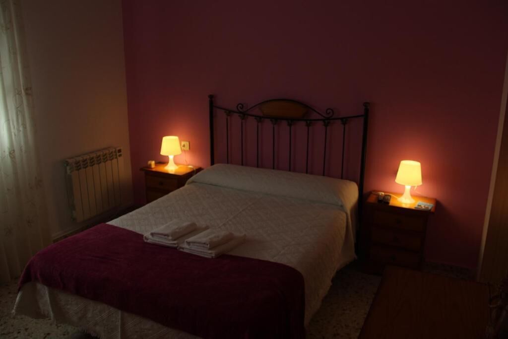 Una habitación con una cama, dos lámparas de noche, un radiador y una ventana con cortinas.