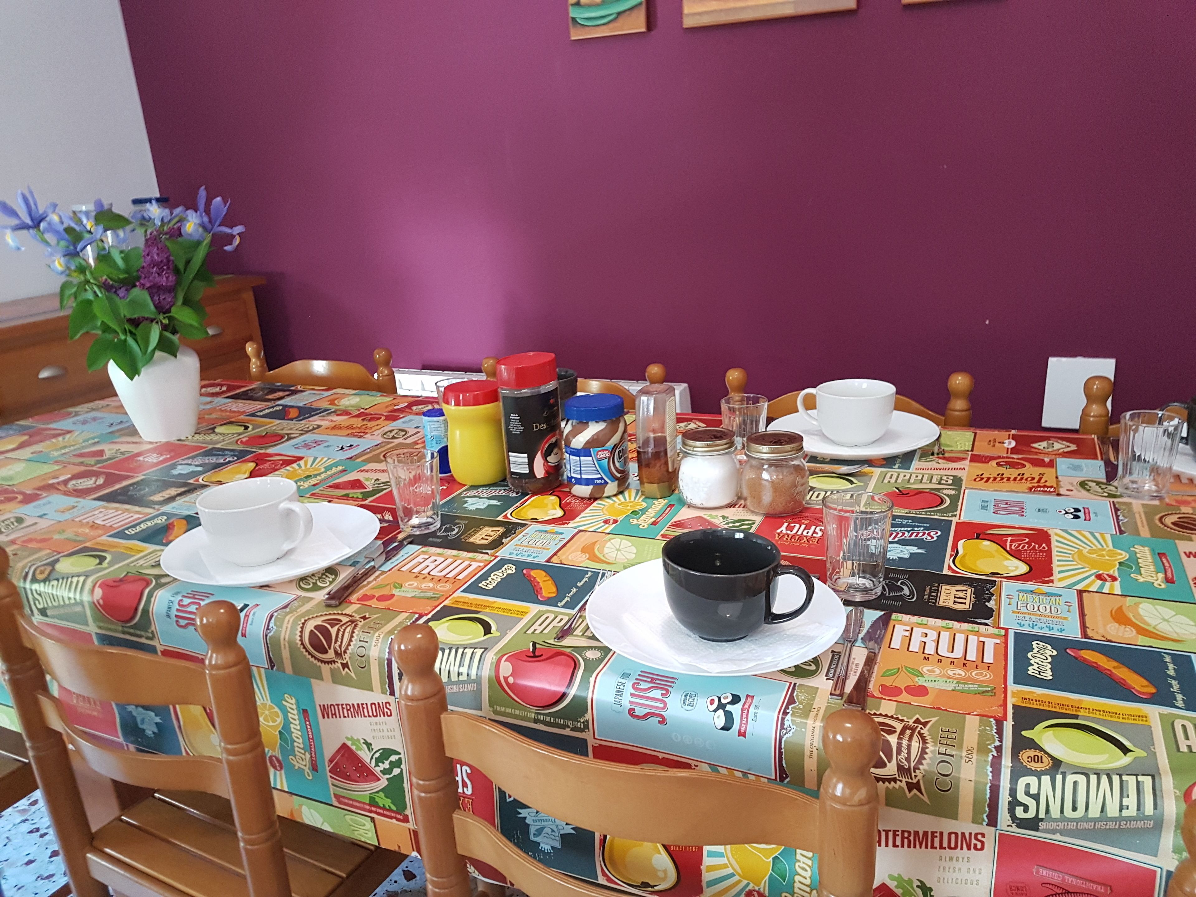 Una mesa de comedor con mantel colorido, diferentes alimentos y una planta en maceta.