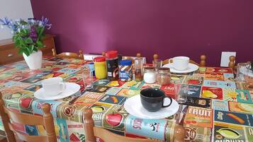 Una mesa de comedor con mantel colorido, diferentes alimentos y una planta en maceta.