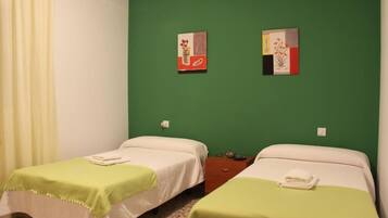 Ein Zimmer mit zwei Betten, jedes mit einer grünen Tagesdecke und weißen Bettwäsche, sowie zwei an der Wand hängenden Kunstwerken.