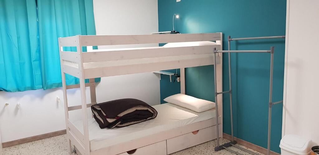 Un lit superposé avec un bureau et une chaise, une petite étagère et une fenêtre avec des rideaux.