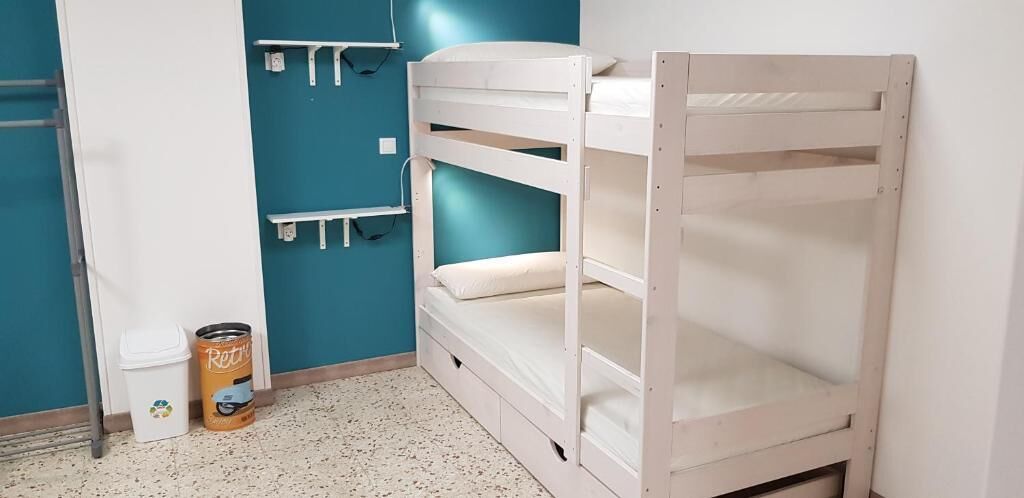 A bunk bed room with a blue wall, a white trash bin, and a recycling bin.